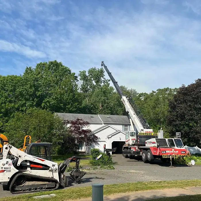crane over house with tree branches being disposed in front yard